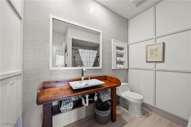 bathroom featuring a shower with shower curtain, toilet, sink, and tile walls