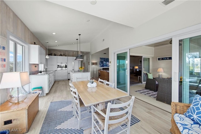 dining area featuring sink, light hardwood / wood-style floors, and high vaulted ceiling