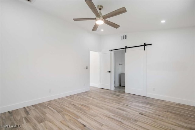 empty room with lofted ceiling, a barn door, ceiling fan, and light wood-type flooring