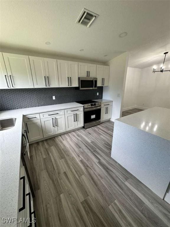 kitchen with pendant lighting, white cabinetry, tasteful backsplash, hardwood / wood-style flooring, and stainless steel appliances