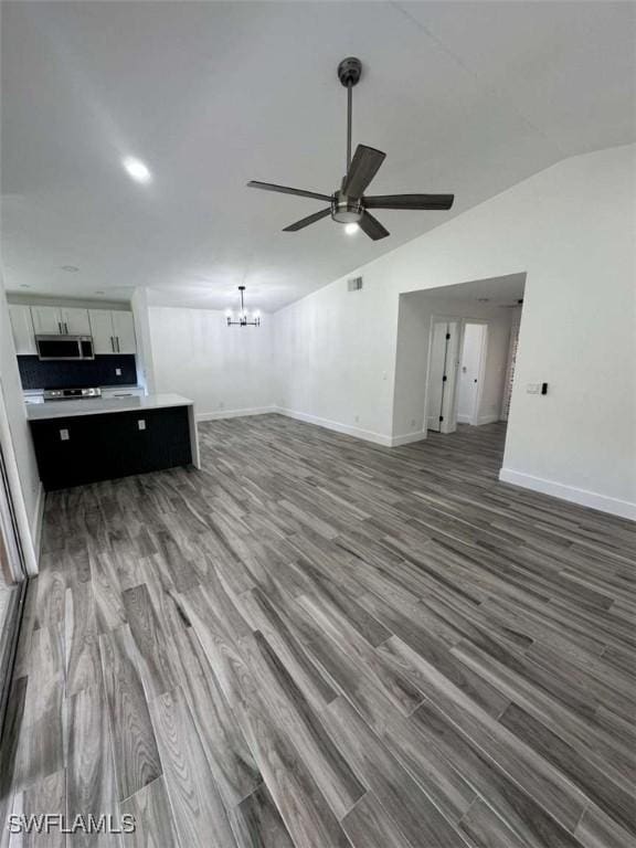 unfurnished living room with dark wood-type flooring, lofted ceiling, and ceiling fan with notable chandelier