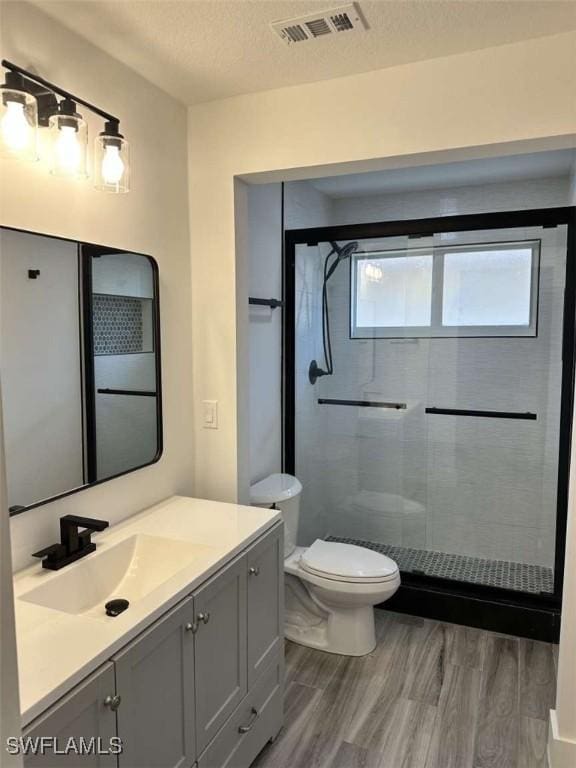 bathroom with toilet, a textured ceiling, vanity, a shower with door, and hardwood / wood-style flooring