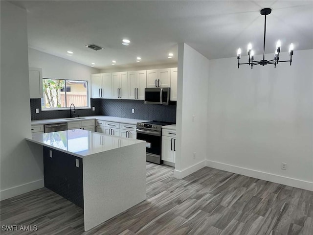 kitchen featuring white cabinetry, hanging light fixtures, stainless steel appliances, light hardwood / wood-style floors, and decorative backsplash