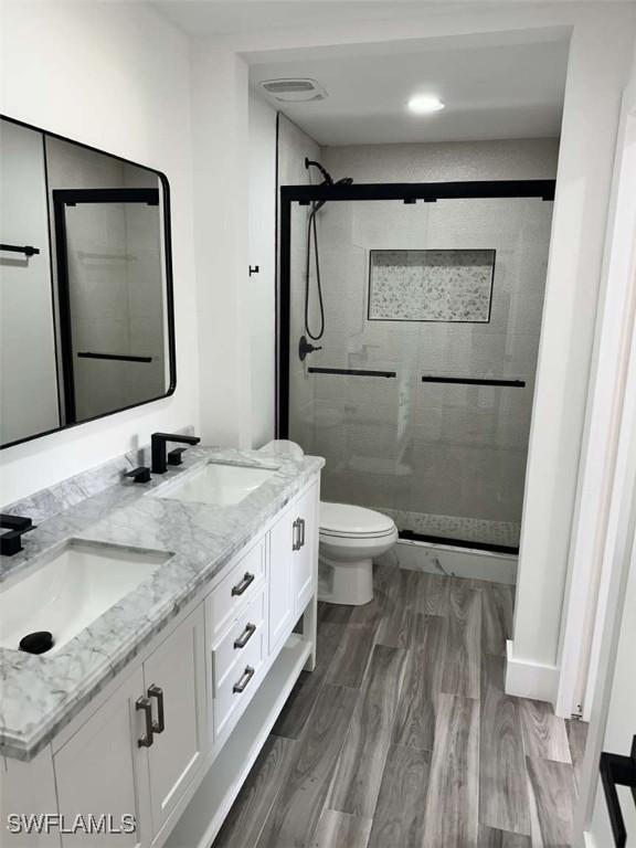 bathroom with vanity, wood-type flooring, toilet, and a tile shower