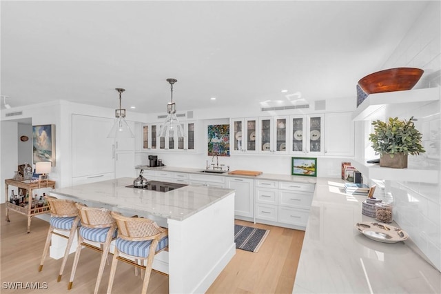 kitchen with hanging light fixtures, white cabinetry, a kitchen island, and glass insert cabinets