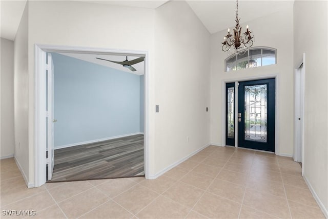 foyer entrance with light tile patterned floors, baseboards, high vaulted ceiling, and ceiling fan with notable chandelier