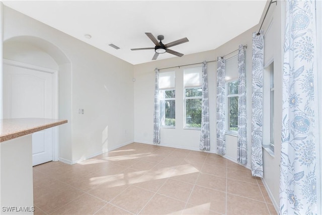 empty room with light tile patterned floors, arched walkways, visible vents, baseboards, and a ceiling fan