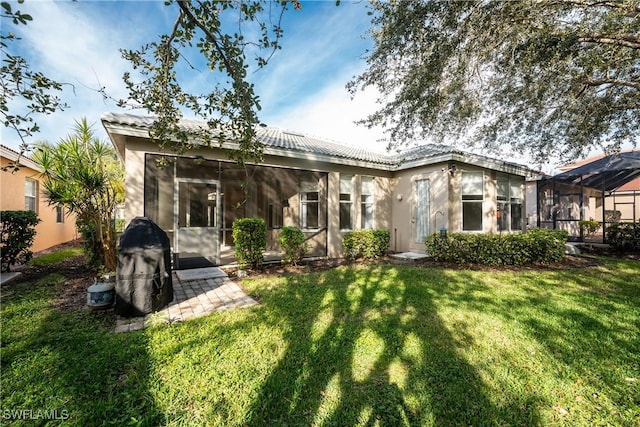 back of house with a sunroom, a lawn, a tiled roof, and stucco siding