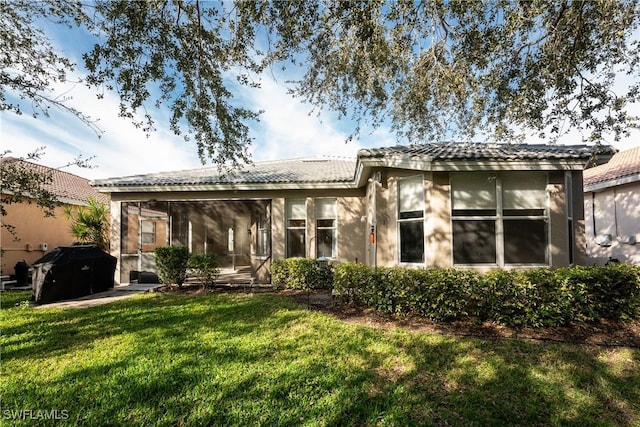 back of property with a sunroom, a tile roof, a yard, and stucco siding