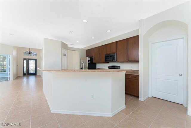 kitchen featuring light tile patterned floors, stainless steel fridge, a notable chandelier, a center island with sink, and french doors