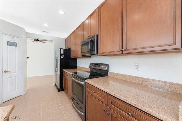 kitchen featuring light tile patterned floors, brown cabinetry, ceiling fan, light stone counters, and stainless steel appliances