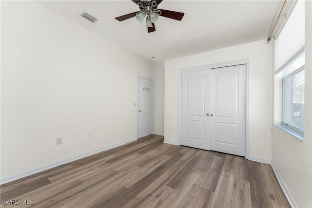 unfurnished bedroom featuring ceiling fan, wood finished floors, visible vents, baseboards, and a closet