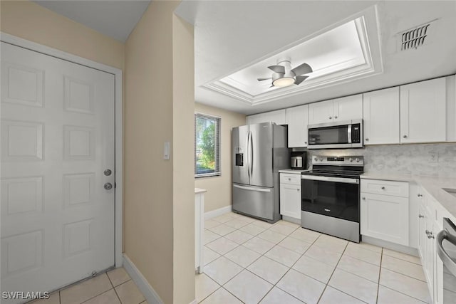 kitchen with a raised ceiling, white cabinets, ceiling fan, stainless steel appliances, and backsplash