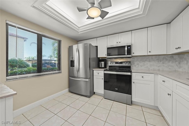 kitchen featuring appliances with stainless steel finishes, white cabinets, decorative backsplash, light tile patterned floors, and a tray ceiling