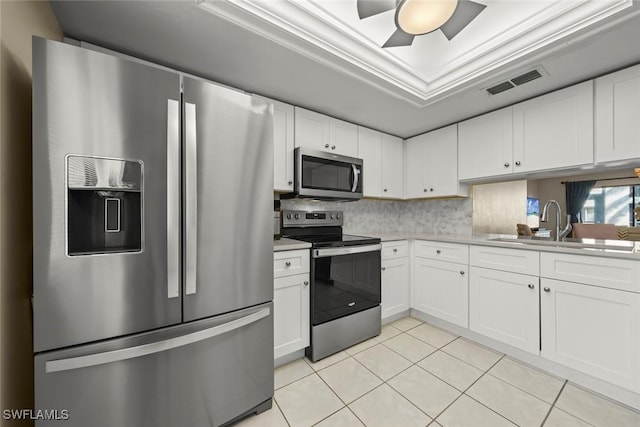 kitchen with light tile patterned flooring, sink, white cabinets, a tray ceiling, and stainless steel appliances