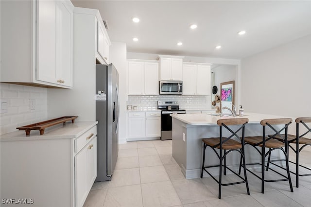 kitchen with sink, white cabinetry, stainless steel appliances, an island with sink, and a kitchen bar