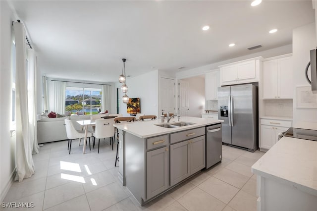 kitchen with appliances with stainless steel finishes, sink, white cabinets, hanging light fixtures, and a center island with sink