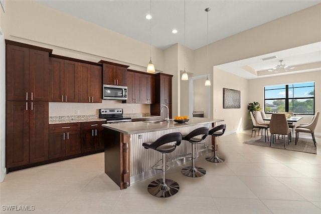 908 SW Embers Ter, Cape Coral, FL 33991 - kitchen with stainless steel microwave, electric stove, light countertops, a breakfast bar area, and a center island with sink