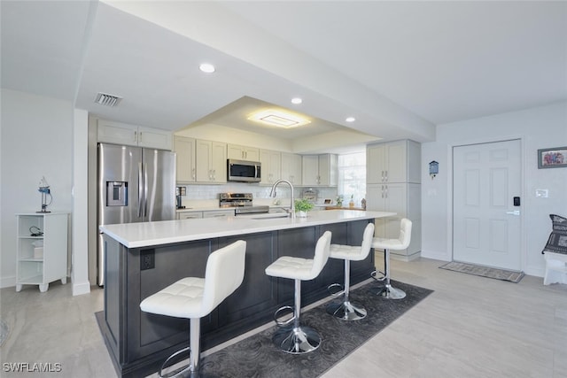 kitchen featuring decorative backsplash, stainless steel appliances, a breakfast bar area, and a center island with sink