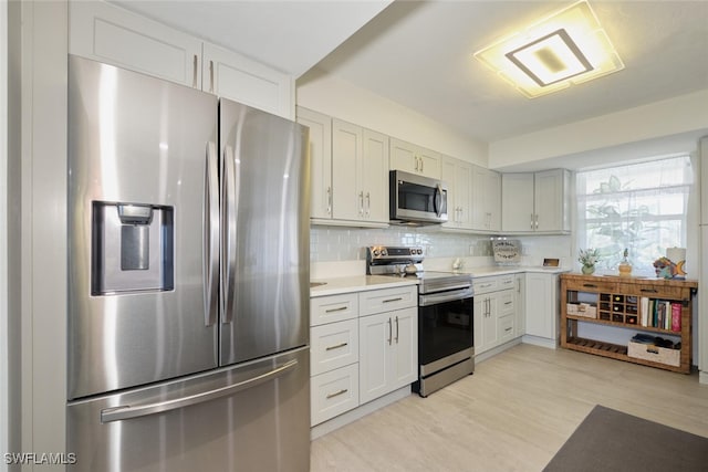 kitchen with tasteful backsplash, white cabinetry, light hardwood / wood-style flooring, and appliances with stainless steel finishes