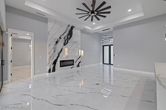 unfurnished living room featuring a tray ceiling, a large fireplace, ceiling fan, and french doors