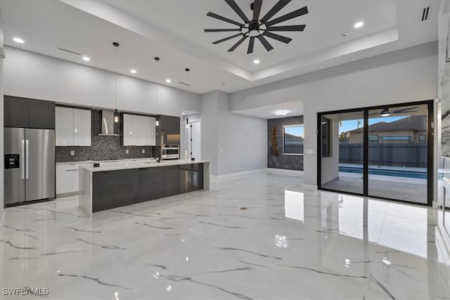 kitchen featuring appliances with stainless steel finishes, pendant lighting, white cabinets, a center island with sink, and wall chimney exhaust hood