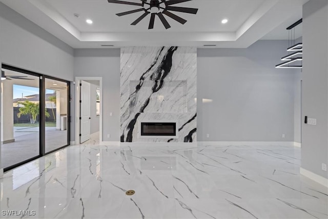 unfurnished living room featuring a tray ceiling, a fireplace, and ceiling fan