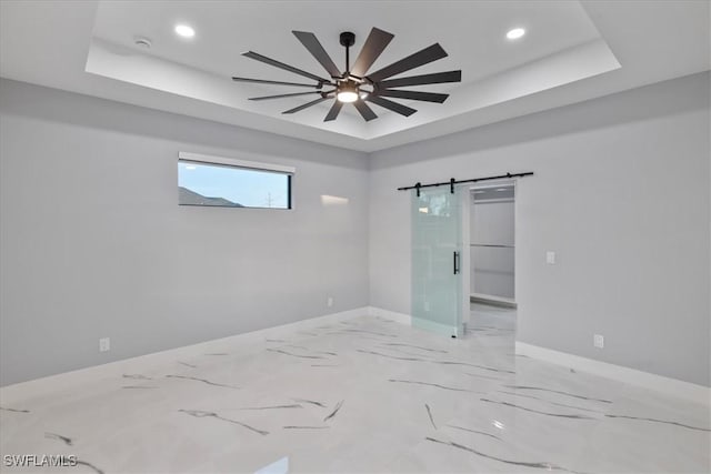 unfurnished room featuring a raised ceiling, a barn door, and ceiling fan