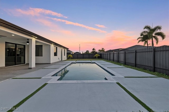 pool at dusk featuring ceiling fan and a patio area