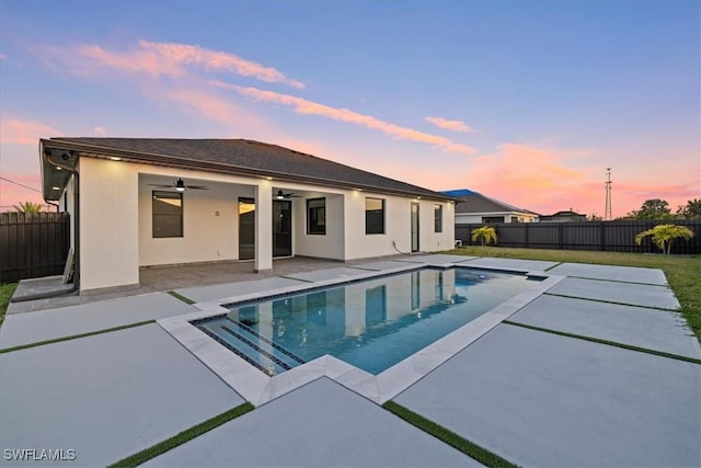 pool at dusk featuring ceiling fan and a patio area