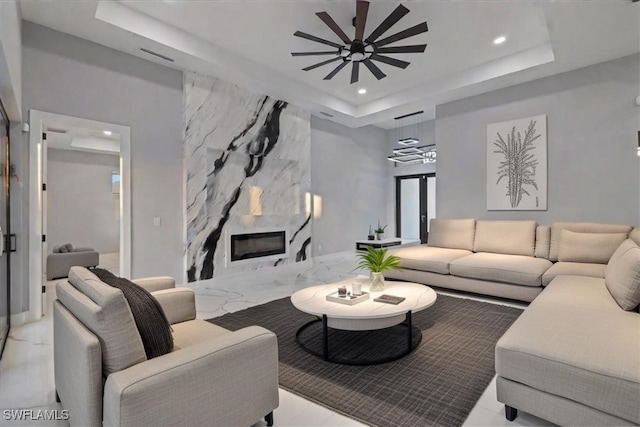 living room featuring ceiling fan, a fireplace, and a tray ceiling