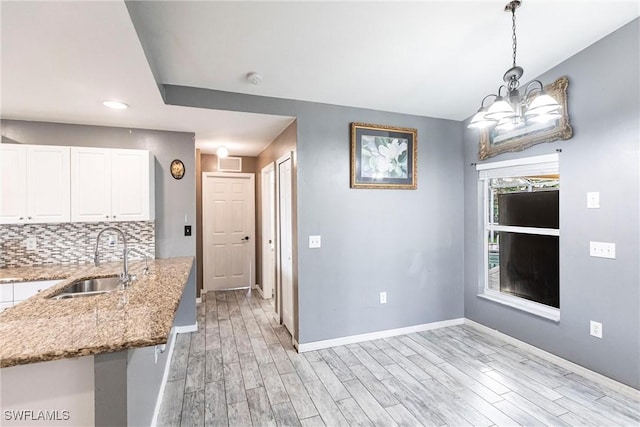 kitchen featuring tasteful backsplash, sink, white cabinets, hanging light fixtures, and light hardwood / wood-style flooring