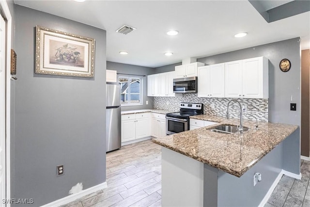 kitchen with sink, kitchen peninsula, stainless steel appliances, light stone countertops, and white cabinets