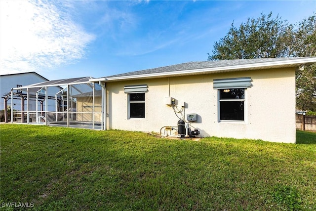 rear view of house with glass enclosure and a lawn