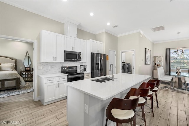 kitchen with appliances with stainless steel finishes, white cabinetry, an island with sink, sink, and a kitchen breakfast bar