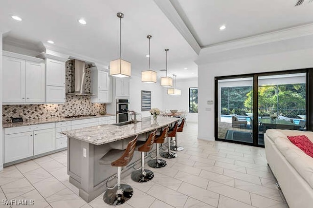 kitchen featuring a kitchen island with sink, white cabinets, and wall chimney exhaust hood