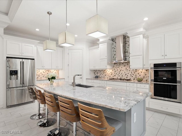 kitchen featuring a breakfast bar, sink, appliances with stainless steel finishes, an island with sink, and wall chimney range hood