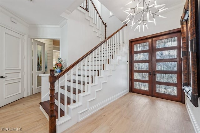 entrance foyer with ornamental molding, light hardwood / wood-style flooring, a notable chandelier, and french doors