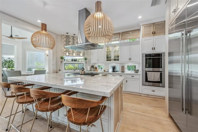 kitchen featuring white cabinetry, a center island, island exhaust hood, stainless steel appliances, and light stone countertops