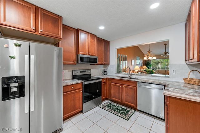 kitchen with light stone counters, light tile patterned floors, stainless steel appliances, brown cabinetry, and a sink