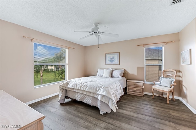 bedroom with a textured ceiling, ceiling fan, dark wood-style flooring, visible vents, and baseboards