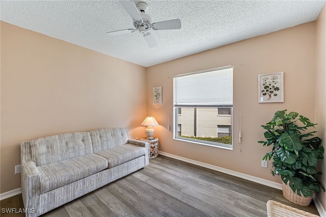 living area featuring a textured ceiling, baseboards, and wood finished floors