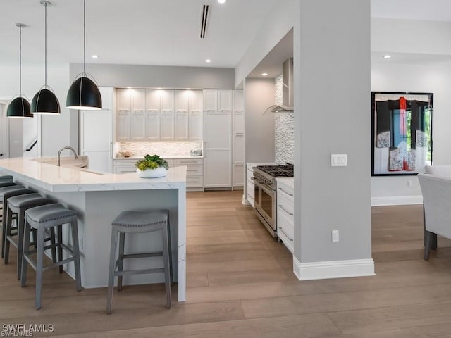 kitchen with wall chimney range hood, a kitchen breakfast bar, white cabinets, decorative light fixtures, and range with two ovens