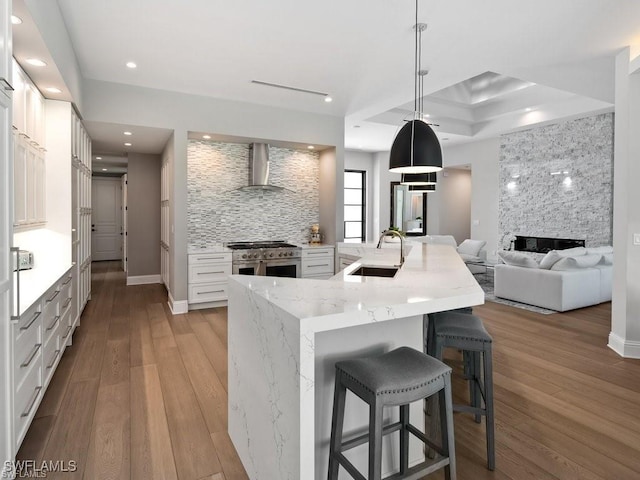 kitchen with wall chimney exhaust hood, a kitchen bar, sink, hanging light fixtures, and range with two ovens