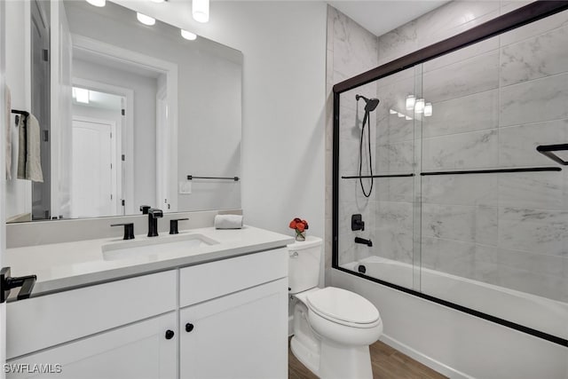 full bathroom with hardwood / wood-style flooring, vanity, combined bath / shower with glass door, and toilet