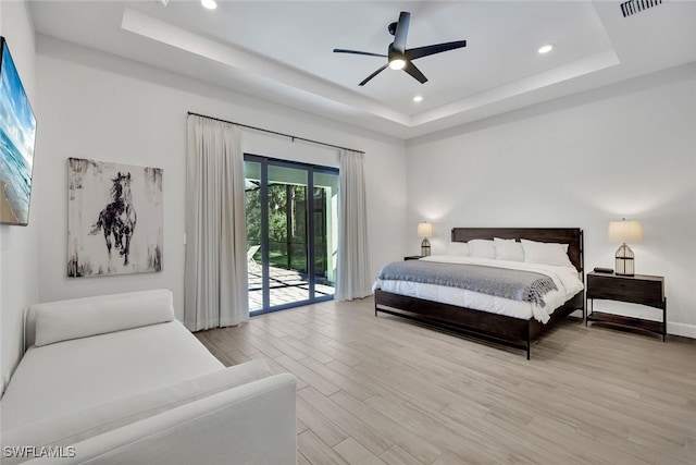 bedroom with ceiling fan, access to exterior, a raised ceiling, and light wood-type flooring