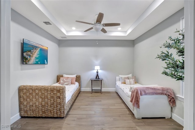 bedroom with a raised ceiling, ceiling fan, and light wood-type flooring