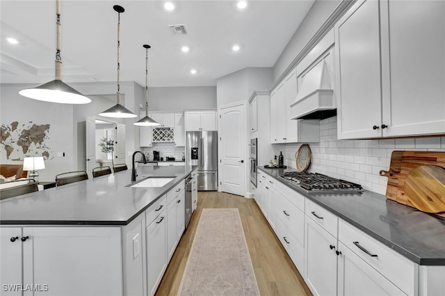 kitchen featuring a large island, sink, premium range hood, stainless steel appliances, and decorative light fixtures