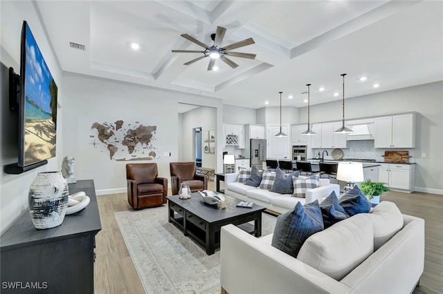 living room featuring coffered ceiling, ceiling fan, light hardwood / wood-style flooring, and beamed ceiling