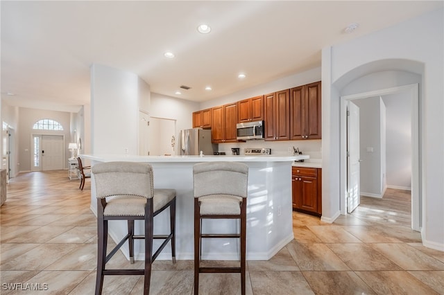 kitchen featuring stainless steel appliances, light tile patterned flooring, a kitchen island, and a breakfast bar area